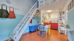A kitchen with a red and white tiled floor, a blue counter, and a red and white tiled backsplash. There is a staircase with white railings leading to an upper level. - Casa Celeste in Pomonte (Marciana)