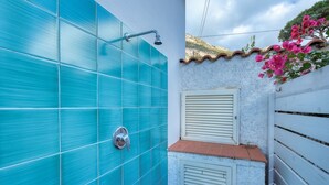 A bathroom with blue tiles, a showerhead, and a window with shutters. - Casa Celeste in Pomonte (Marciana)