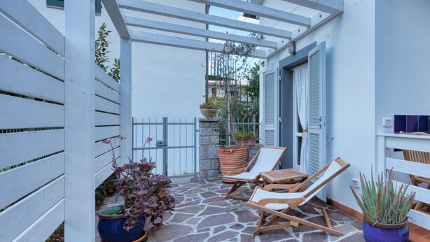 A covered patio with stone flooring, two wooden lounge chairs, and potted plants. - Casa Celeste in Pomonte (Marciana)