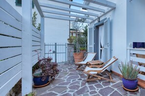A covered patio with stone flooring, two wooden lounge chairs, and potted plants. - Casa Celeste in Pomonte (Marciana)