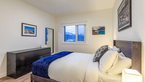 A bedroom with a bed, a dresser, a window with a mountain view, and framed pictures on the wall. - Modern 2BR in Golden w/ Stunning  MTN Views! (Golden)