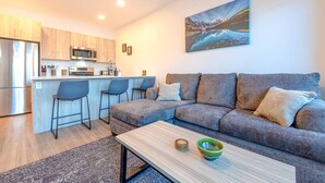 A modern living room with a grey sofa, a coffee table, and a kitchen area with wooden cabinets and a microwave. - Modern 2BR in Golden w/ Stunning  MTN Views! (Golden)
