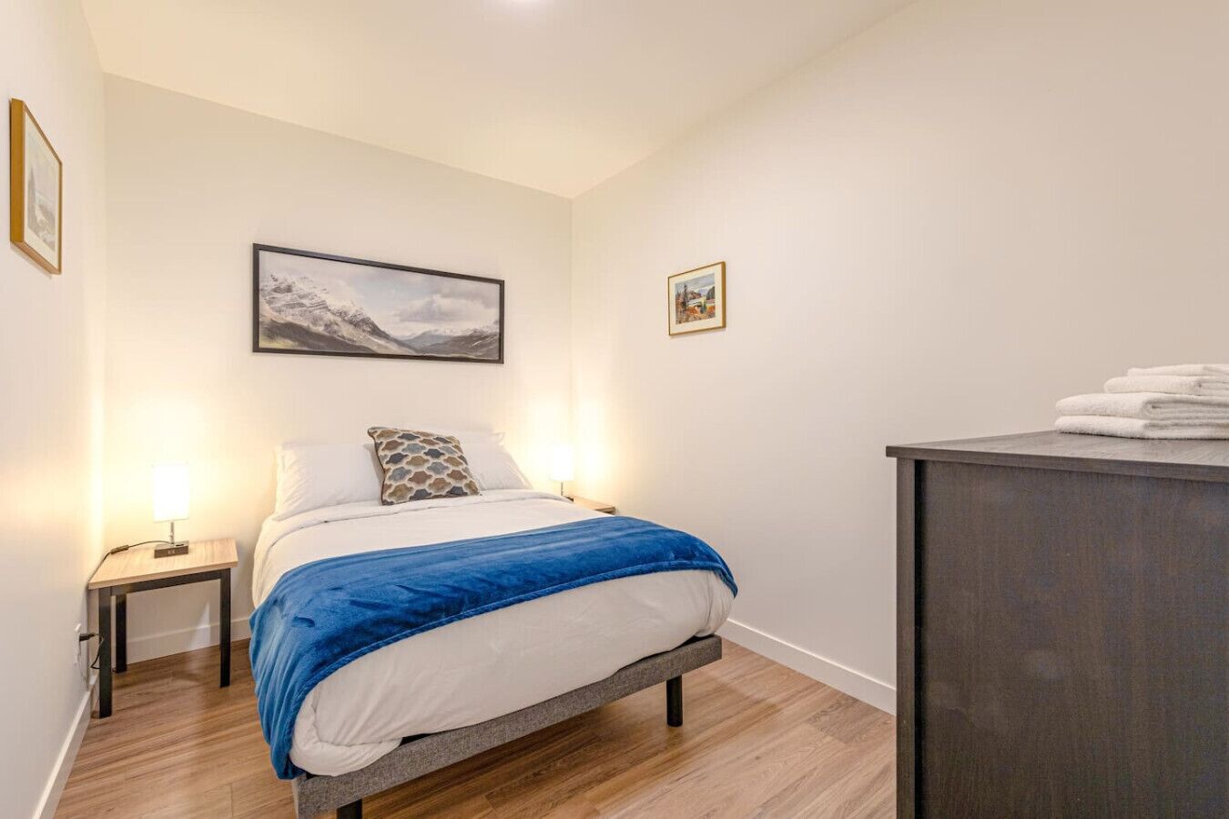 Une chambre à coucher comprenant un lit, deux tables de chevet, une commode, une coiffeuse et deux tableaux encadrés accrochés au mur.