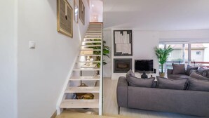 Un salon moderne avec un escalier blanc, un canapé gris et un téléviseur à écran plat.