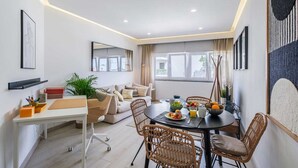 A modern living room with a dining area, featuring a sofa set, a dining table with fruit and drinks, and a large window with a view. - Sea View in Estoril by Portugal Portfolio (Estoril)