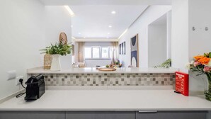 A modern kitchen with a white countertop, a tiled backsplash, and a black coffee maker. There is a potted plant on the counter and a red sign on the wall. - Sea View in Estoril by Portugal Portfolio (Estoril)
