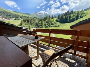 A wooden deck with a table and chairs overlooking a mountainous landscape.