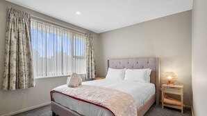 Un dormitorio con una cama grande, una mesita de noche y un ventanal con cortinas.