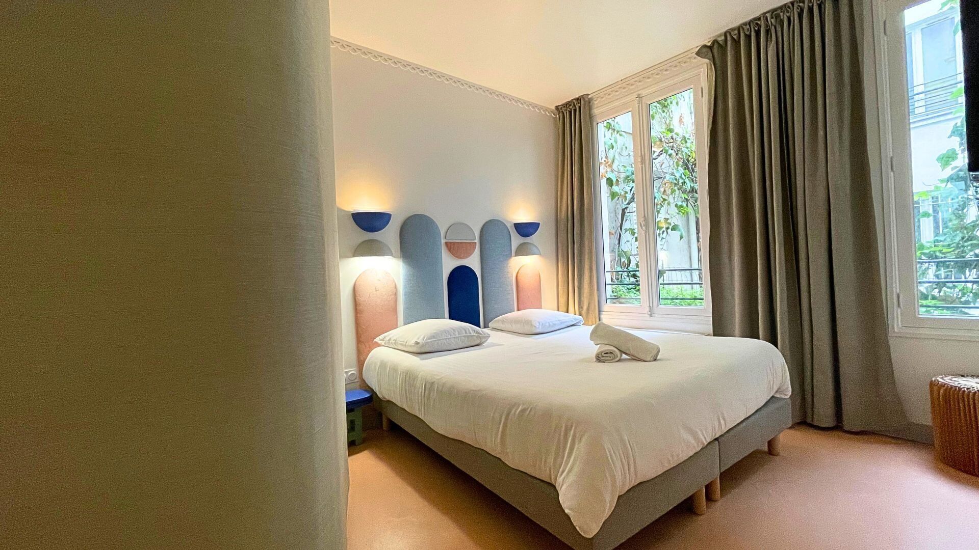 Un dormitorio con cama, lámparas de noche, una ventana con cortinas y vistas al verdor exterior.