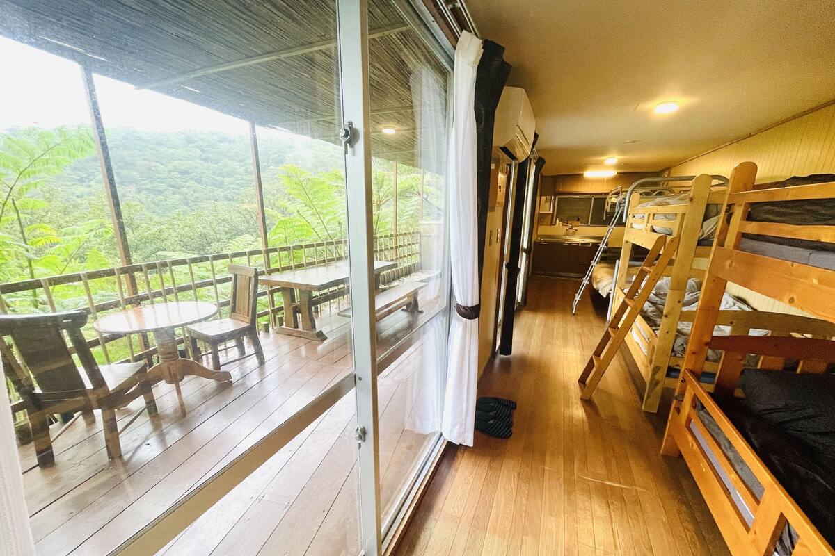 Une cabane avec un plancher en bois, des lits superposés, une table à manger et une vue sur un paysage boisé.