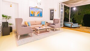 Un salon moderne avec un canapé beige, une table basse et un fauteuil bleu. Un tableau est accroché au mur, et une plante en pot est posée à proximité.