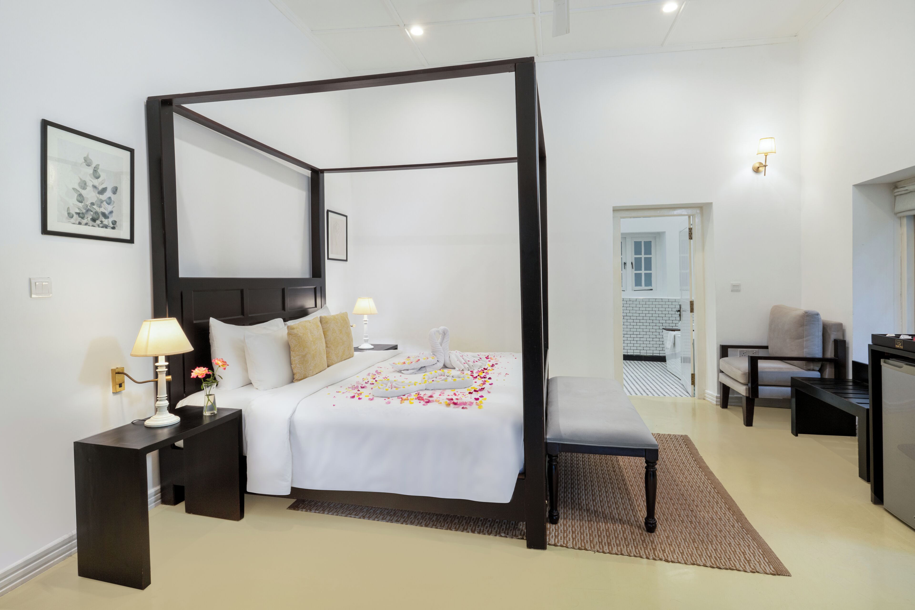 Una cama con dosel, con una colcha y almohadas blancas, una mesita de noche con lámpara y una silla en una habitación de hotel.