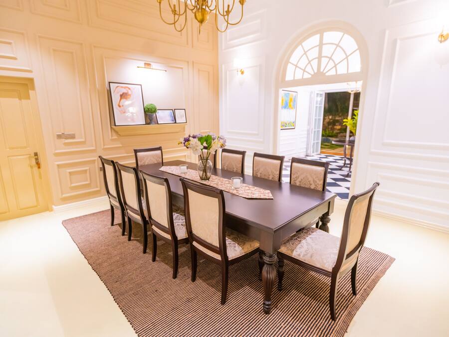 A formal dining room with a dark wooden table, eight upholstered chairs, a patterned runner, and a chandelier.
