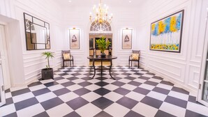 Un hall d’hôtel avec un sol à carreaux, un lustre, des œuvres d’art encadrées et une table centrale entourée de chaises.
