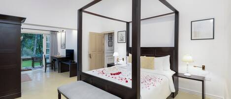 A four-poster bed with rose petals, a desk, and a bench in a hotel room.