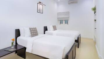 Une chambre d’hôtel avec deux lits, une table de chevet, un tableau encadré au mur, un appareil de climatisation et une fenêtre avec un store.