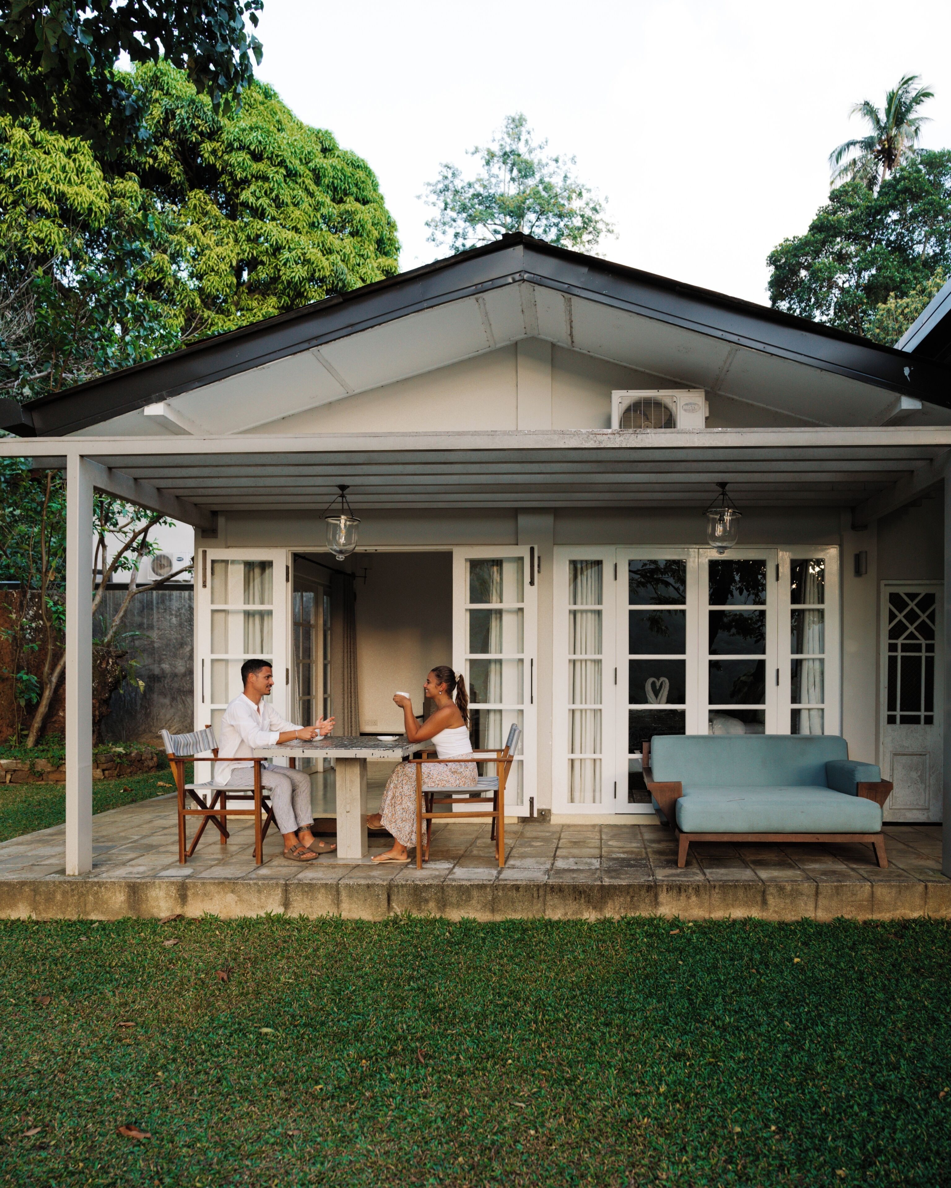 A covered patio with a table and chairs, a sofa, and a person seated at the table.