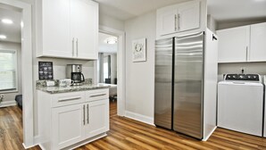 Una cocina moderna con gabinetes blancos, un refrigerador de acero inoxidable, una cafetera y una lavadora.