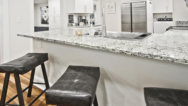 Una cocina moderna con encimera de granito, electrodomésticos de acero inoxidable y dos taburetes de bar.
