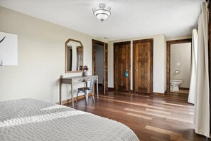 Une chambre à coucher avec un lit, un bureau et une chaise, un miroir, des portes en bois et un luminaire au plafond.