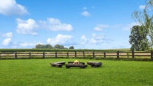 A grassy field with a wooden fence, a fire pit, and a tree.