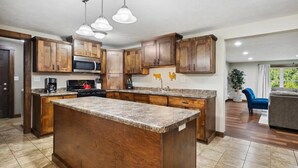A kitchen with wooden cabinets, a granite countertop island, a microwave, and pendant lighting.