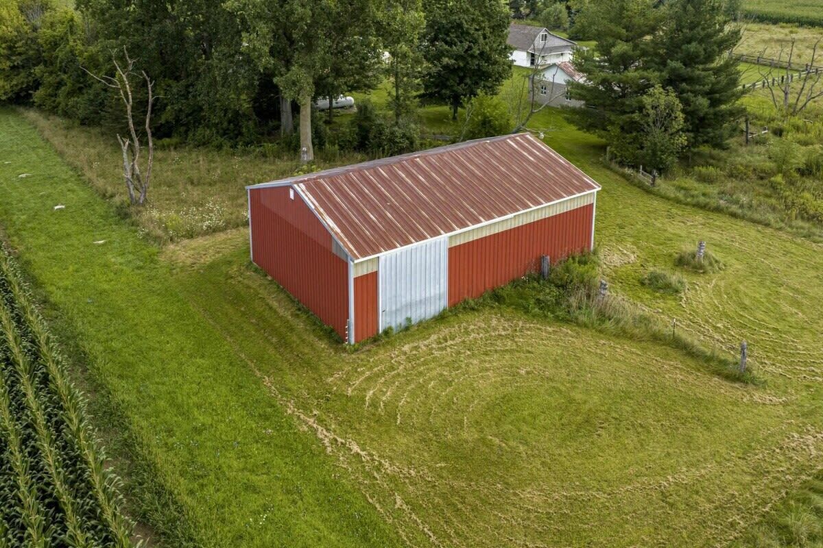 Et rødt metalskur med en hvid dør i en græsmark med træer og et hus i baggrunden.