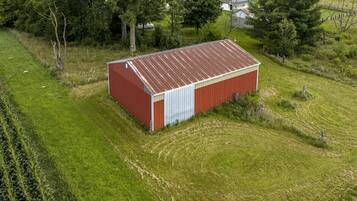 Et rødt metalskur med en hvid dør i en græsmark med træer og et hus i baggrunden.