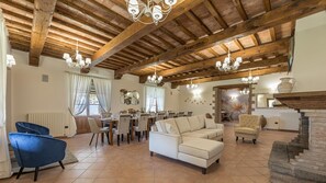 A spacious living area with a high wooden ceiling, a dining area, and a staircase leading to an upper level. - Tenuta Montiepoli 12 3 Emma Villas (Valfabbrica)