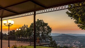 An outdoor dining area with tables, chairs, and a view of the countryside at sunset. - Tenuta Montiepoli 12 3 Emma Villas (Valfabbrica)