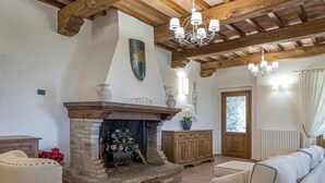 A living room with a fireplace, wooden beams, and a chandelier. - Tenuta Montiepoli 12 3 Emma Villas (Valfabbrica)