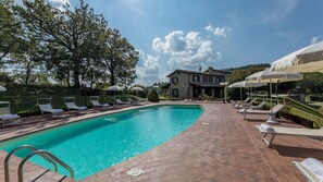 A swimming pool with lounge chairs and umbrellas, surrounded by a stone building and trees. - Tenuta Montiepoli 12 3 Emma Villas (Valfabbrica)