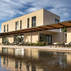 Un bâtiment moderne doté d’une piscine, de chaises longues et d’un patio couvert.