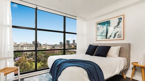 A bedroom with a large window, a bed, a bedside table, and a city view. - Darlinghurst — Newly renovated 1BR + Parking (City of Sydney)