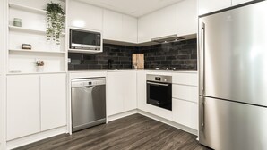 A modern kitchen with white cabinetry, a stainless steel refrigerator, a dishwasher, an oven, and a microwave. - Darlinghurst — Newly renovated 1BR + Parking (City of Sydney)