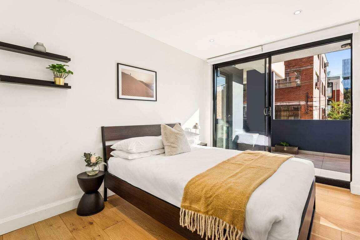 A modern bedroom with a bed, bedside tables, a window with a view, and a sliding glass door leading to an outdoor area.