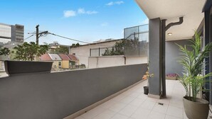 Een balkon met tegels, een plant in pot en uitzicht op omliggende gebouwen.