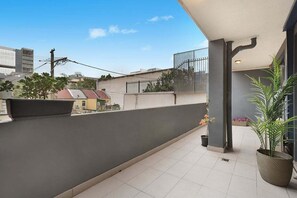 Een balkon met tegels, een plant in pot en uitzicht op omliggende gebouwen.