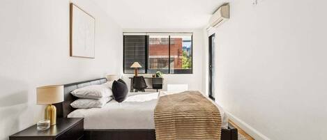 A modern bedroom with a bed, bedside table, lamp, and a view of the outside.