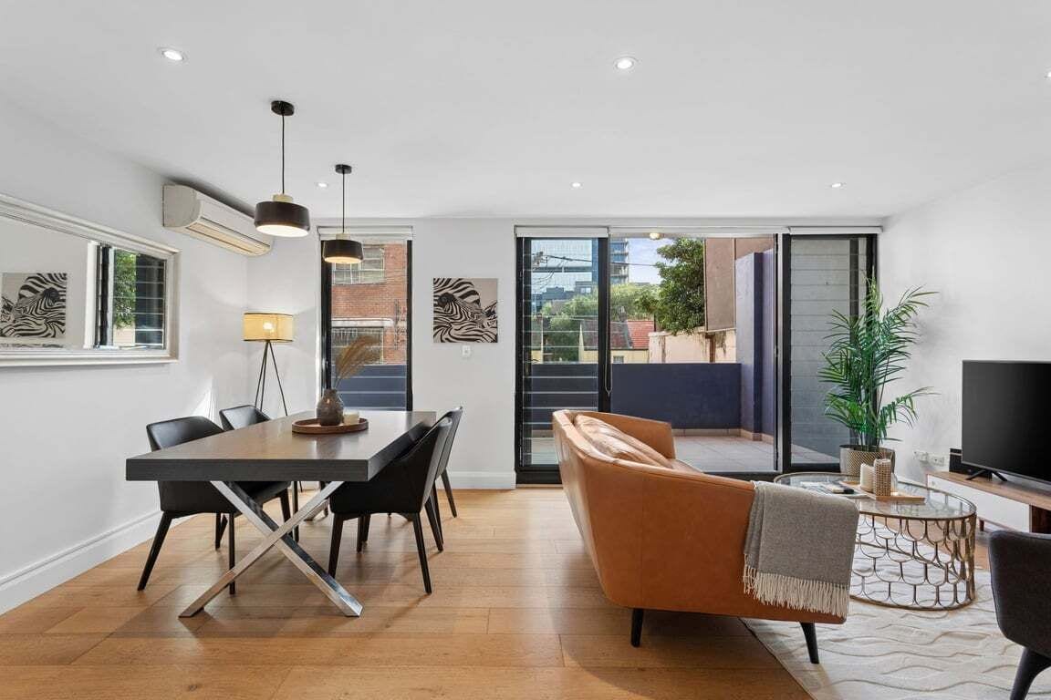 A modern living room with a dining area, a sofa, a TV, and a balcony with a view.