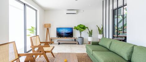 A modern living room with a green sofa, wooden chairs, a coffee table, and a television.