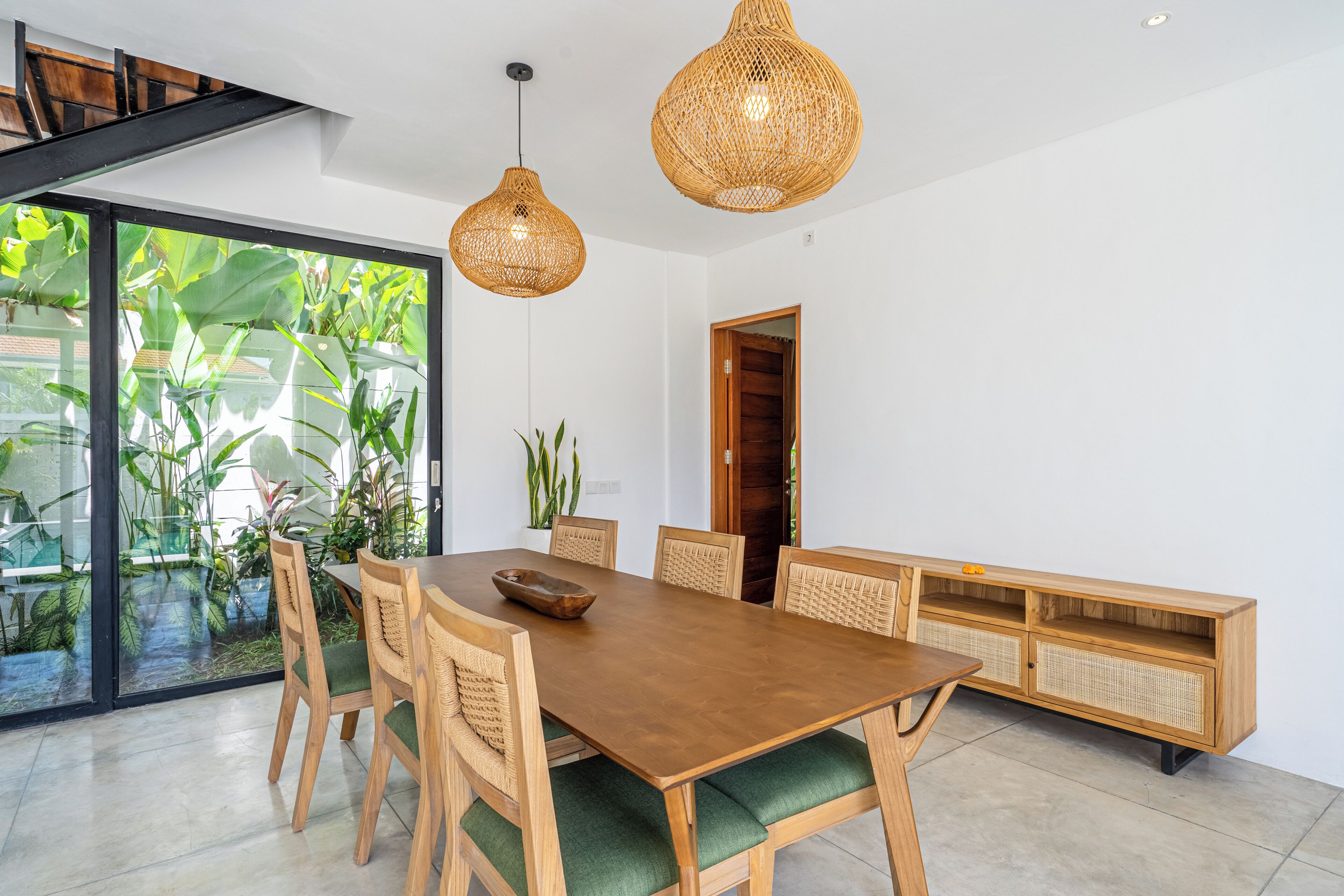 A dining area with a wooden table, green cushioned chairs, and wicker pendant lights.