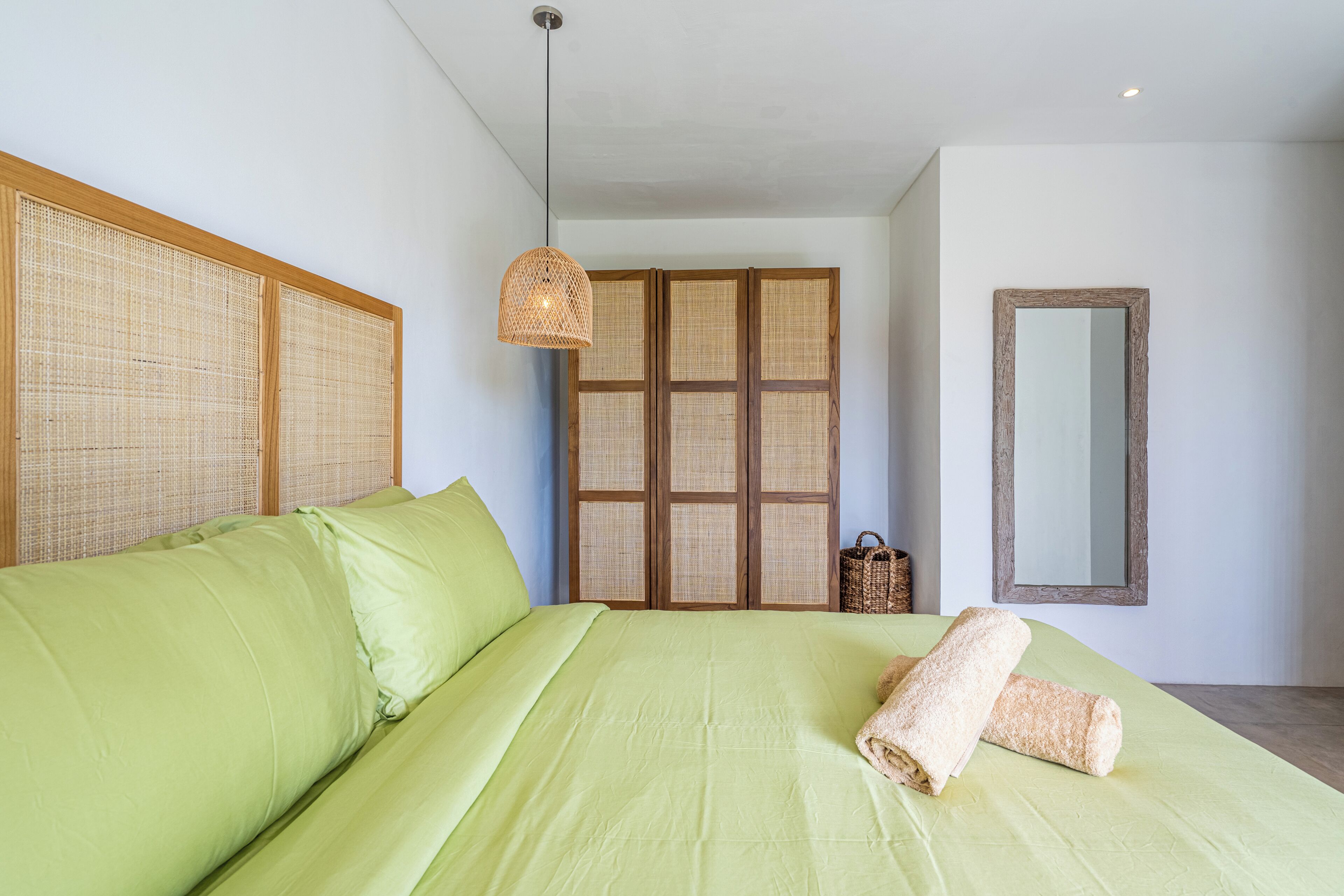 Un dormitorio con una cama grande, un cabecero tejido, una lámpara colgante, un separador tejido y un espejo en la pared.