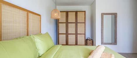 A bedroom with a large bed, a woven headboard, a hanging light fixture, a woven partition, and a mirror on the wall.