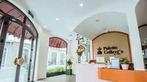 A reception area with a sign reading "Palette Collect's," a reception desk, a potted plant, and a view of the street outside. - Palette Collect's Boutique Hotel Ha Long (Bai Chay)