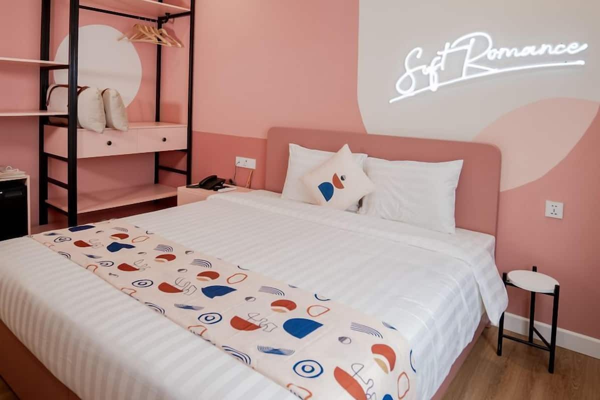 Ein Schlafzimmer mit Etagenbett, Nachttisch, Beistelltisch, Bett mit gemustertem Überwurf sowie einer Wand mit einer Neonreklame und einem kleinen Hocker.