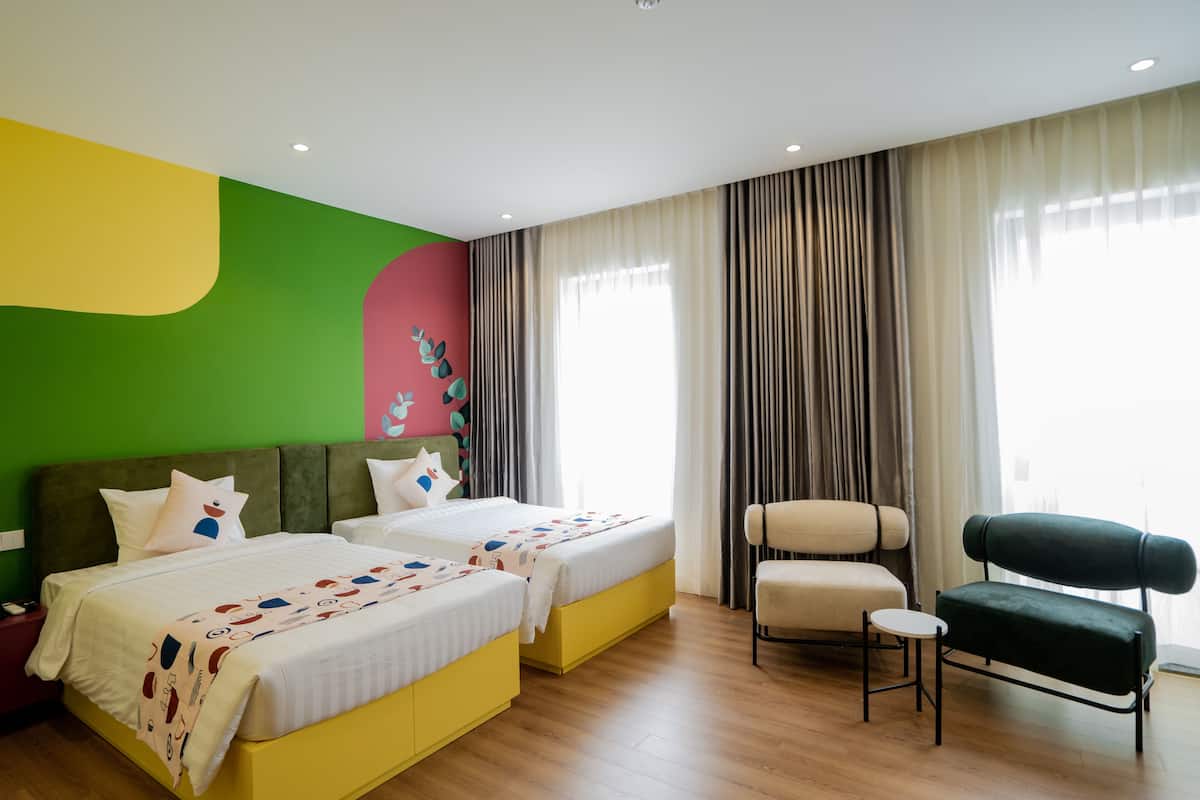 Ein Hotelzimmer mit zwei Betten, einem Sessel, einem kleinen Tisch und einem großen Fenster mit Vorhängen.