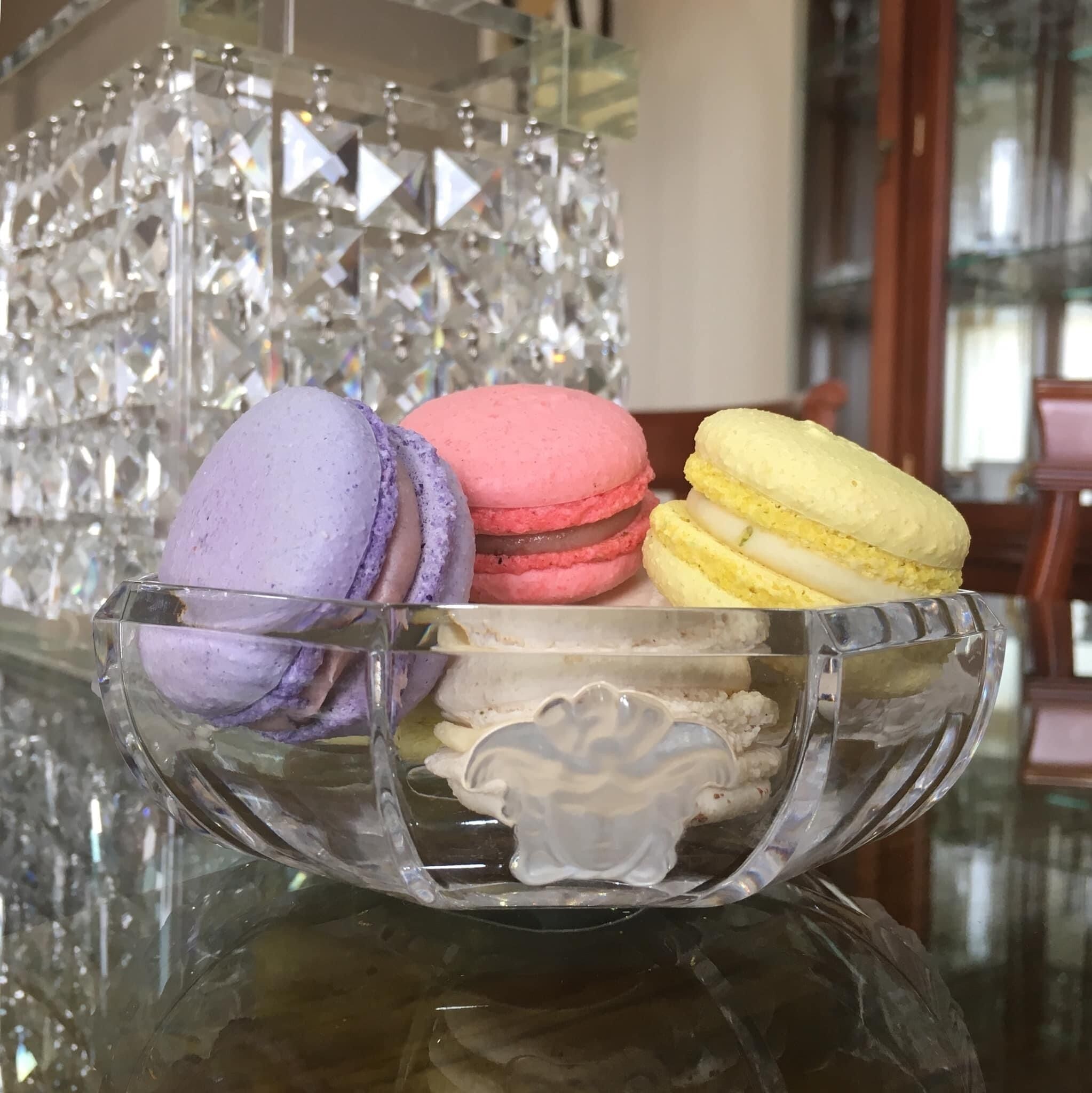 A glass bowl containing three macarons on a reflective surface.