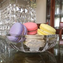 Un cuenco de vidrio con tres macarons sobre una superficie reflectante.