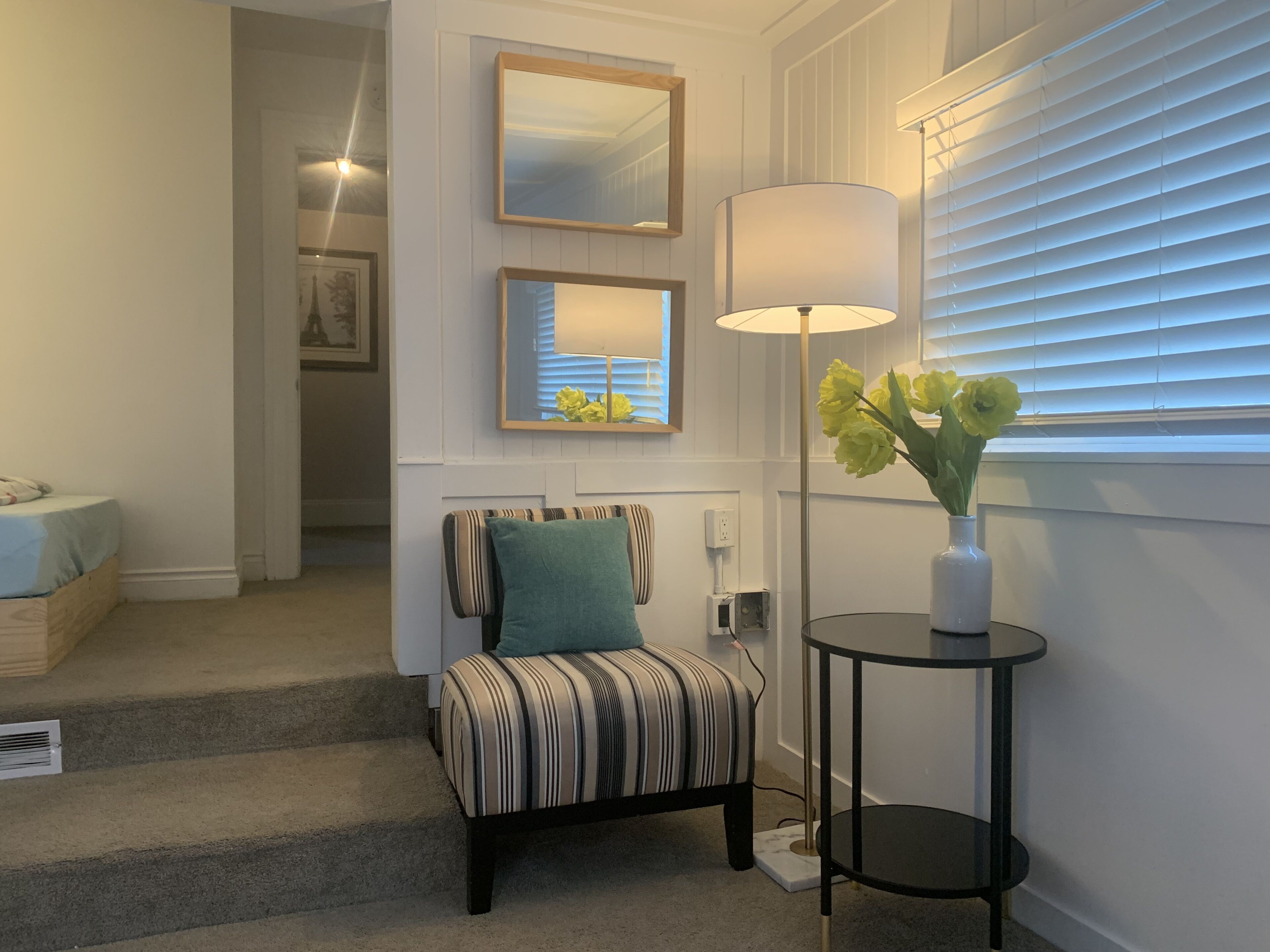 A room with a striped chair, a small table with a vase of flowers, and a lamp.